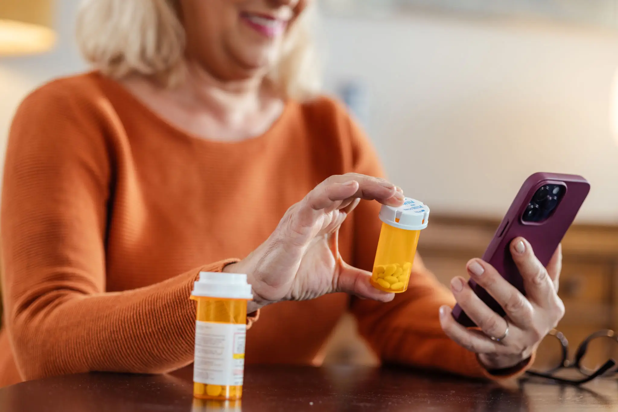 Senior woman checking prescription bottle with smartphone