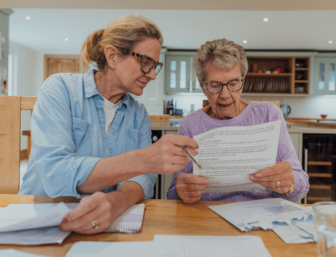 Elderly woman reading paper with assistance.
