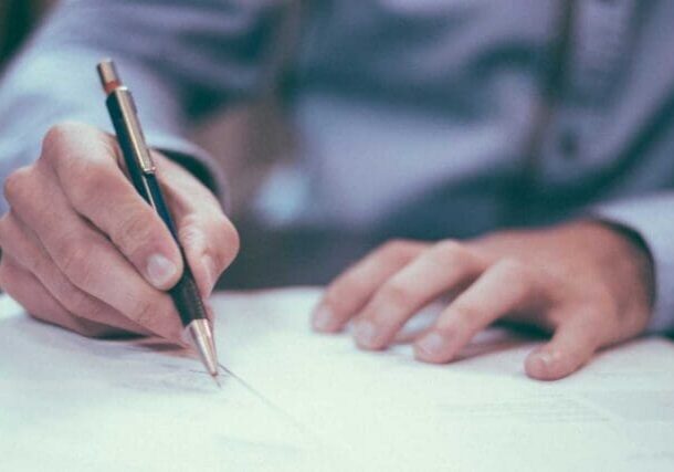 Person writing on paper with pen